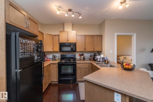 The kitchen features light wood cabinetry, black appliances, track lighting, and a double basin sink - 416 263 Macewan Road, Edmonton, AB - Indoor Photo Showing Kitchen With Double Sink