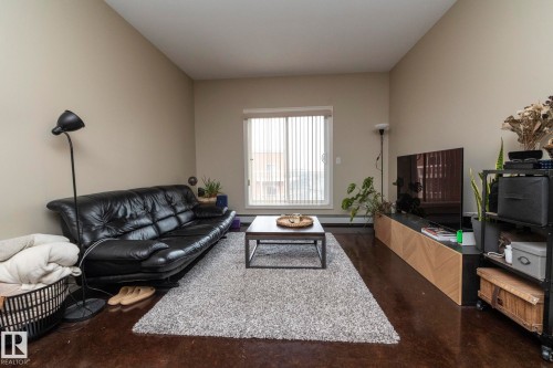 Living area with light-colored walls, dark flooring, and a large window with vertical blinds - 416 263 Macewan Road, Edmonton, AB - Indoor Photo Showing Living Room