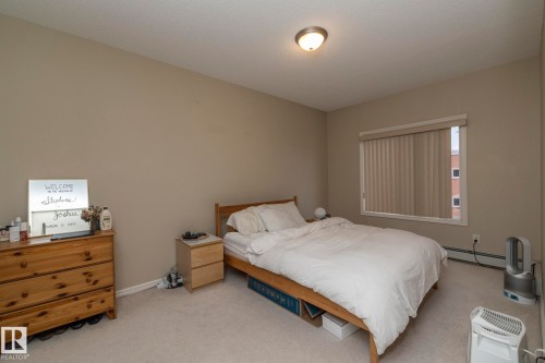 The room features light-colored walls and carpeting, a window with vertical blinds, and a ceiling-mounted light fixture - 416 263 Macewan Road, Edmonton, AB - Indoor Photo Showing Bedroom
