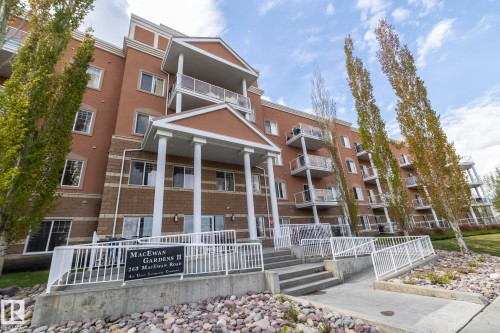 The property features a multi-story building with balconies, a main entrance with columns, and a ramp for accessibility - 416 263 Macewan Road, Edmonton, AB - Outdoor With Balcony With Facade