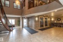 The property features a spacious lobby with tile flooring, a curved staircase with dark wood and wrought iron railings, and two elevators with stainless steel doors - 416 263 Macewan Road, Edmonton, AB  - Indoor Photo Showing Other Room 
