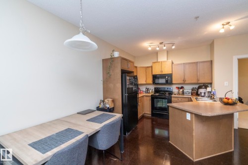 Well-appointed kitchen featuring light wood cabinetry, black appliances, a double basin sink, and an island with an extended countertop for dining - 416 263 Macewan Road, Edmonton, AB - Indoor Photo Showing Kitchen With Double Sink
