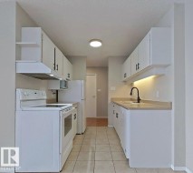 Kitchen featuring white appliances, under cabinet range hood, light countertops, white cabinets, and a textured ceiling - 