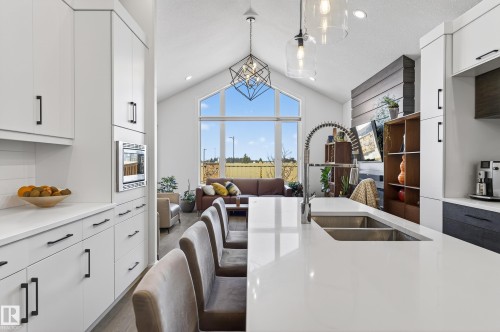 Well-appointed kitchen featuring a large island with seating, a double basin sink with a gooseneck faucet, white cabinetry with black hardware, and an integrated microwave - 45 Evermore Crescent, St. Albert, AB - Indoor Photo Showing Kitchen With Double Sink
