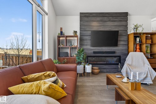 The living area features large windows, wood-look flooring, and a modern fireplace with a wall-mounted television above - 45 Evermore Crescent, St. Albert, AB - Indoor Photo Showing Living Room With Fireplace