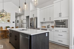 The kitchen features a large island with a stainless steel sink and dishwasher, white quartz countertops, and dark wood cabinetry - 