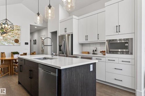 The kitchen features a large island with a stainless steel sink and dishwasher, white quartz countertops, and dark wood cabinetry - 45 Evermore Crescent, St. Albert, AB - Indoor Photo Showing Kitchen With Double Sink With Upgraded Kitchen