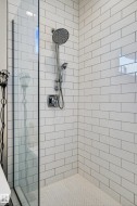 The shower features white subway tile walls, a glass enclosure, and a chrome shower head with an additional handheld shower fixture - 
