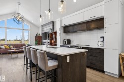 The kitchen features a large island with a white countertop and seating for four, modern cabinetry in white and dark wood finishes, and stainless steel appliances - 