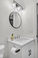 The bathroom features a vanity with a white countertop and an integrated sink, complemented by a round mirror and a three-light fixture above - 