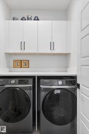 Laundry area featuring white cabinetry with dark hardware, a white countertop, and dark-colored front-loading appliances - 