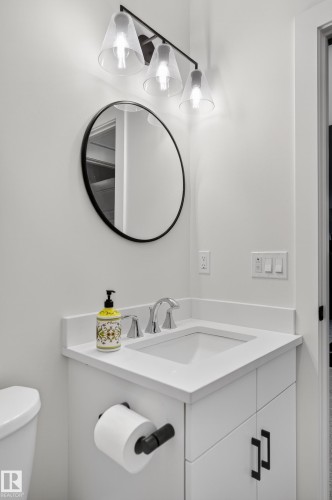 The bathroom features a vanity with a white countertop and an integrated sink, complemented by a round mirror and a three-light fixture above - 45 Evermore Crescent, St. Albert, AB - Indoor Photo Showing Bathroom