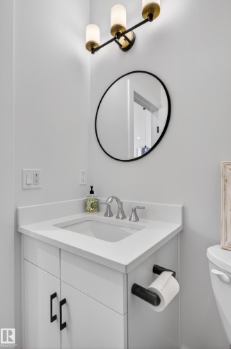 The bathroom features a modern vanity with a white countertop and an integrated sink, complemented by a round mirror and contemporary wall-mounted lighting - 45 Evermore Crescent, St. Albert, AB - Indoor Photo Showing Bathroom