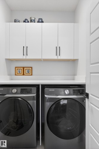 Laundry area featuring white cabinetry with dark hardware, a white countertop, and dark-colored front-loading appliances - 45 Evermore Crescent, St. Albert, AB - Indoor Photo Showing Laundry Room