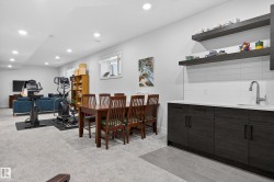 This versatile area features a wet bar with dark wood cabinetry, white countertop, and tiled backsplash - 