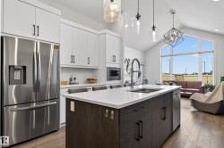 The kitchen features white cabinetry, a stainless steel refrigerator, and a kitchen island with a sink and seating - 