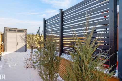 The property features a dark-colored horizontal slat fence, a light-colored outdoor storage shed, and various plantings, all set against a clear sky - 45 Evermore Crescent, St. Albert, AB - Outdoor