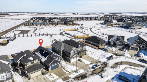 Aerial view showcasing a residential area with varied home designs, paved roads, and a snow-covered open field with walking paths - 45 Evermore Crescent, St. Albert, AB - Outdoor With View