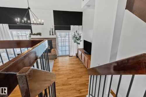 The property features hardwood floors, a stone fireplace, and large windows with white curtains - 17082 67 Avenue Nw, Edmonton, AB - Indoor Photo Showing Other Room