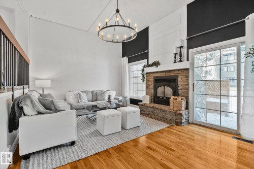 Living area featuring hardwood floors, a stone fireplace, and a sliding glass door providing access to the outdoors - 17082 67 Avenue Nw, Edmonton, AB - Indoor Photo Showing Living Room With Fireplace