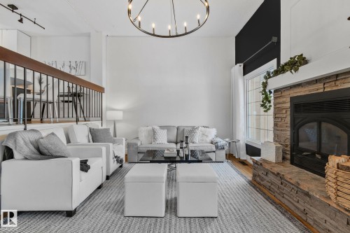 Living area featuring a stone fireplace, a large window, a prominent chandelier, and a partial view of an upper-level railing - 17082 67 Avenue Nw, Edmonton, AB - Indoor Photo Showing Living Room With Fireplace