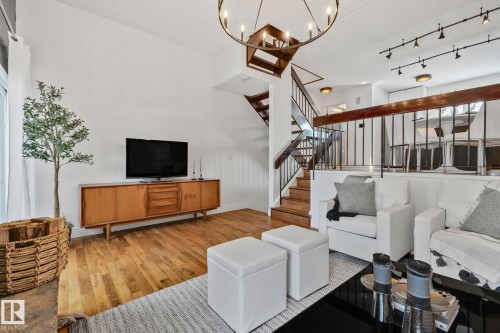 Spacious living area featuring hardwood flooring, a prominent staircase with dark wood handrails and black balusters, and a decorative chandelier - 17082 67 Avenue Nw, Edmonton, AB - Indoor Photo Showing Living Room