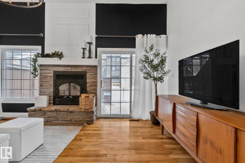 Living area featuring hardwood floors, a stone fireplace, and a glass sliding door - 17082 67 Avenue Nw, Edmonton, AB - Indoor Photo Showing Living Room With Fireplace