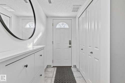 The property entrance features a white door with an arched window, tile flooring, and white bifold doors - 17082 67 Avenue Nw, Edmonton, AB - Indoor Photo Showing Other Room
