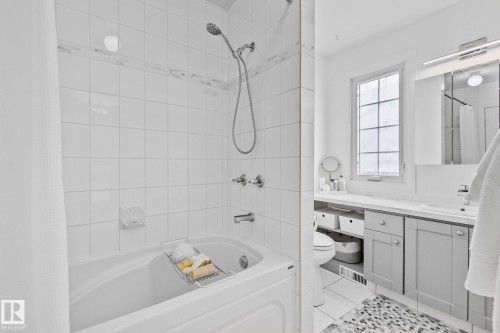 Bathroom featuring white tiled walls, a shower-bath combination, and a vanity with a white countertop and gray cabinetry - 17082 67 Avenue Nw, Edmonton, AB - Indoor Photo Showing Bathroom