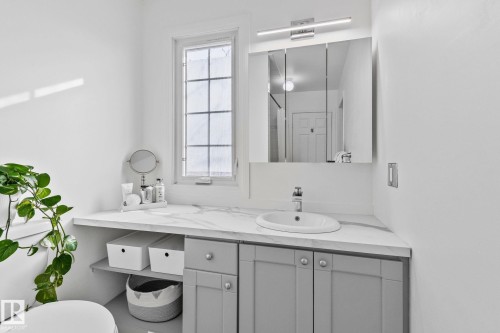 Bathroom vanity featuring a white countertop with a built-in sink, a wall-mounted light fixture, and a mirrored medicine cabinet - 17082 67 Avenue Nw, Edmonton, AB - Indoor Photo Showing Bathroom