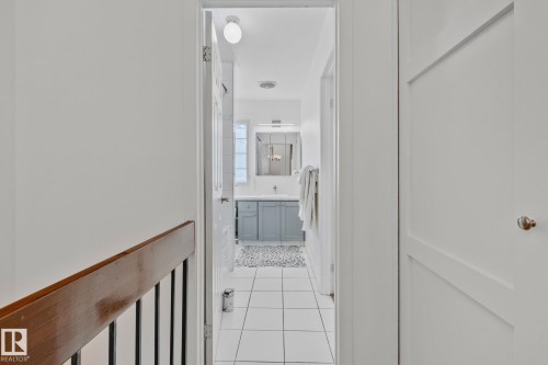 Hallway view leading to a bathroom featuring white tile flooring, a light gray vanity with a white countertop, and a mirrored medicine cabinet - 17082 67 Avenue Nw, Edmonton, AB - Indoor Photo Showing Other Room