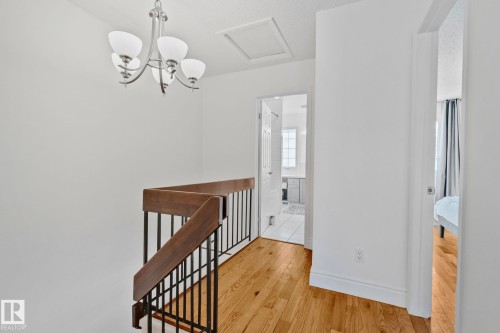 The property features a staircase with wooden handrails and black balusters, leading to a hallway with hardwood flooring - 17082 67 Avenue Nw, Edmonton, AB - Indoor Photo Showing Other Room