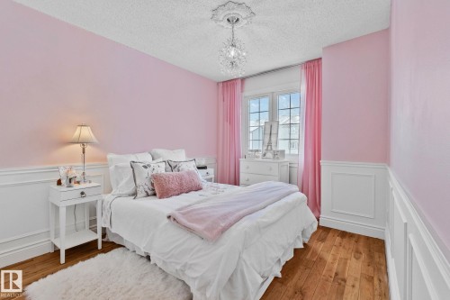 This room features hardwood floors, light pink walls with white wainscoting, and a window with pink curtains - 17082 67 Avenue Nw, Edmonton, AB - Indoor Photo Showing Bedroom
