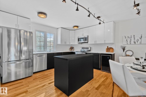 This kitchen features sleek white upper cabinetry and contrasting black lower cabinetry, stainless steel appliances, and a central island with a dark countertop - 17082 67 Avenue Nw, Edmonton, AB - Indoor Photo Showing Kitchen With Stainless Steel Kitchen With Upgraded Kitchen