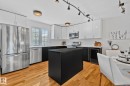 This kitchen features sleek white upper cabinetry and contrasting black lower cabinetry, stainless steel appliances, and a central island with a dark countertop - 17082 67 Avenue Nw, Edmonton, AB  - Indoor Photo Showing Kitchen With Stainless Steel Kitchen With Upgraded Kitchen 