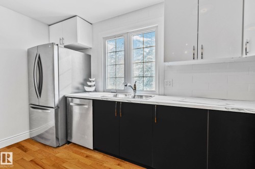 The kitchen features stainless steel appliances, a double sink, black lower cabinetry, white upper cabinetry, and a white subway tile backsplash - 17082 67 Avenue Nw, Edmonton, AB - Indoor Photo Showing Kitchen With Double Sink
