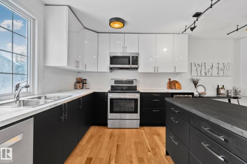 The kitchen features hardwood floors, a stainless steel oven and microwave, and track lighting - 17082 67 Avenue Nw, Edmonton, AB - Indoor Photo Showing Kitchen With Stainless Steel Kitchen With Double Sink With Upgraded Kitchen