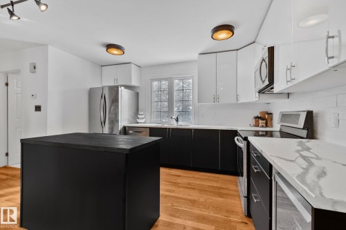 The kitchen features a central island, stainless steel appliances, white upper cabinetry, and contrasting dark lower cabinetry - 17082 67 Avenue Nw, Edmonton, AB - Indoor Photo Showing Kitchen With Stainless Steel Kitchen With Upgraded Kitchen