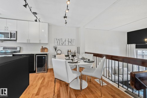 The open concept living area features hardwood floors, modern track lighting, and a kitchen equipped with stainless steel appliances and white cabinetry - 17082 67 Avenue Nw, Edmonton, AB - Indoor