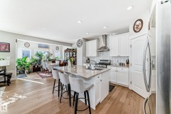 The kitchen features white cabinetry, a stainless steel range hood, a tiled backsplash, and an island with a light-colored countertop - 