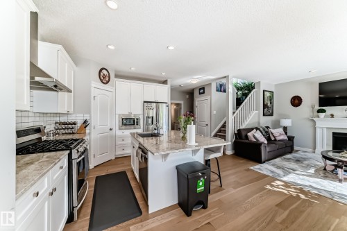 The open concept living area features light hardwood flooring, a kitchen with white cabinetry and stainless steel appliances, and a living room with a white fireplace surround - 22407 99 Avenue, Edmonton, AB - Indoor Photo Showing Kitchen With Stainless Steel Kitchen With Upgraded Kitchen