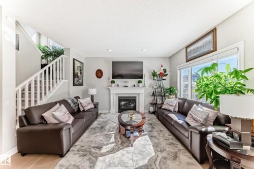 Living area featuring light-colored walls, a prominent fireplace with a white mantel, and large windows providing natural illumination - 22407 99 Avenue, Edmonton, AB - Indoor Photo Showing Living Room With Fireplace