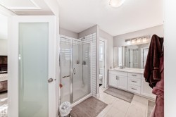The bathroom features a glass-enclosed shower with subway tile surround, a spacious vanity with white cabinetry and a large mirror, and tiled flooring - 
