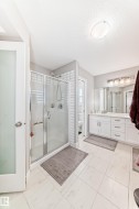 Bathroom featuring a glass-enclosed shower, a double vanity with ample storage, and white tiled flooring - 