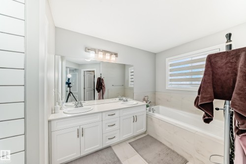 Bathroom featuring a double vanity with white cabinetry and a light-colored countertop, a built-in bathtub, and a window with horizontal blinds - 22407 99 Avenue, Edmonton, AB - Indoor Photo Showing Bathroom