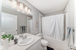 The bathroom features a vanity with an integrated sink, a large mirror with overhead lighting, a bathtub with a shower curtain, and white subway tile accents - 