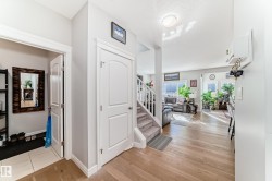 This inviting entryway features light hardwood flooring, a white staircase with carpeted treads, and a convenient closet with a tiled floor - 