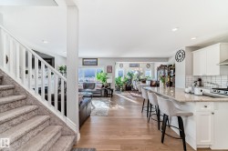 The open concept living area features light hardwood flooring, a kitchen island with seating, and a view into the living room and dining area - 