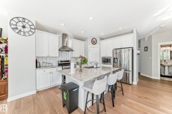 The kitchen features white cabinetry, stainless steel appliances, a white tile backsplash, and a central island with a light-colored countertop - 