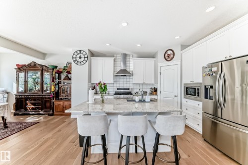 This kitchen features a central island with a granite countertop, white cabinetry, stainless steel appliances, and light-colored hardwood flooring - 22407 99 Avenue, Edmonton, AB - Indoor Photo Showing Kitchen With Stainless Steel Kitchen With Upgraded Kitchen